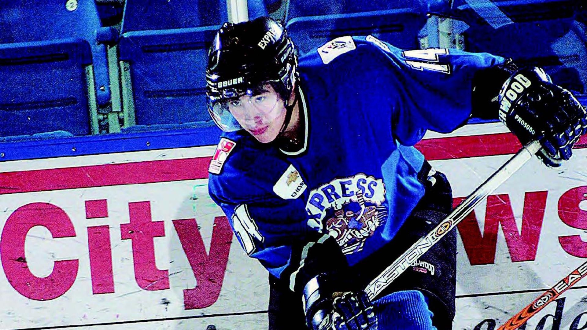 Barndon Yip bends down next to the edge of the rink during a hockey game.